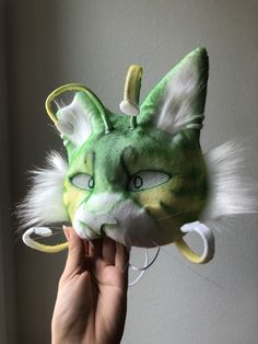 a hand holding up a green and white cat mask