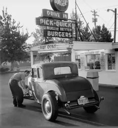 an old car parked in front of a drive - by movie theater with a man fixing it