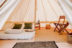 a bed sitting inside of a white tent next to a wooden table and two chairs