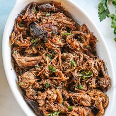 a white bowl filled with shredded meat and garnished with parsley on the side