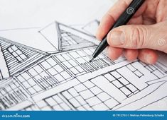 a person's hand holding a pen over architectural drawings