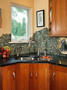 a kitchen with wooden cabinets and black counter tops next to a bowl of fruit on the sink