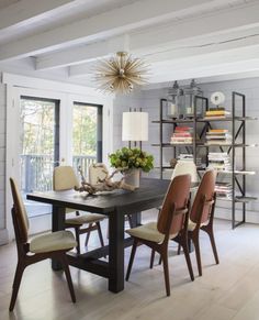 a dining room table with chairs and bookshelves in the back ground, next to an open window