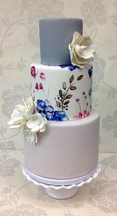 a three tiered cake decorated with flowers on a white tablecloth covered wallpaper