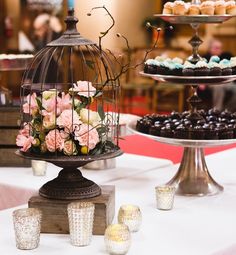 a table topped with cakes and cupcakes covered in frosted icing next to a birdcage filled with flowers