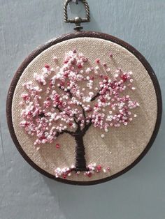 a hand embroidered cherry blossom tree hanging on a wall in a circle with a metal hook