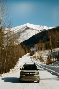 a car driving down a snowy road in front of a snow covered mountainside with trees