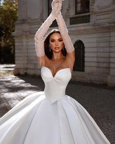 a woman in a white wedding dress is holding her hands up to the side while standing on a cobblestone street