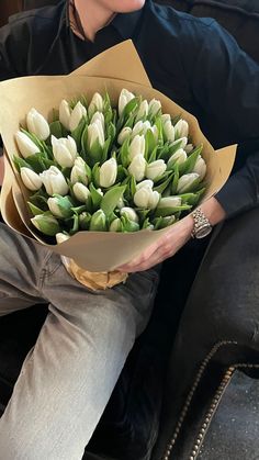 a woman sitting on a couch holding a bouquet of white tulips in her hands