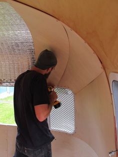 a man with a beer bottle in his hand is painting the inside of a wooden structure