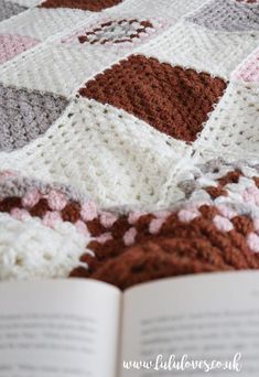 an open book sitting on top of a bed covered in a crocheted blanket