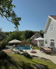 a house with a swimming pool and patio furniture in the back yard, surrounded by lush greenery