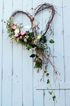 a heart shaped wreath with pink roses and greenery hanging on a white wooden wall