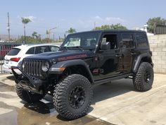 a black jeep parked in a parking lot next to two white cars and a brick wall