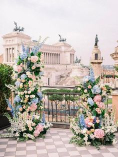 two tall floral arrangements on the ground in front of a building with columns and statues