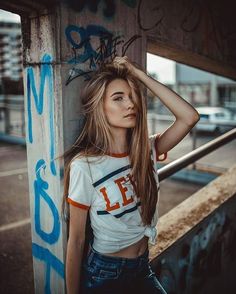 a girl with long hair standing in front of a graffiti covered wall and holding her hand on her head