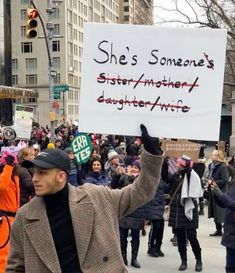 a man holding up a sign that says she's someone's sister / another daughter / wife