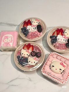 four plates with hello kitty designs and strawberries in them on a marble countertop