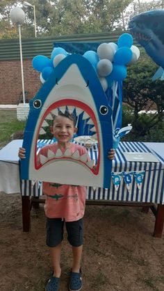 a young boy holding up a shark shaped cardboard cutout in front of a table