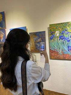 a woman taking a photo of paintings on the wall with her cell phone in hand