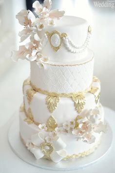 a three tiered wedding cake with white and gold decorations on it's side