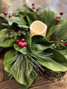 a wreath with red berries and greenery is on a wooden table next to a candle