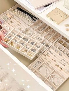 an open drawer filled with jewelry on top of a white table next to other items