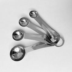 four metal spoons and two silver measuring spoons on a white surface