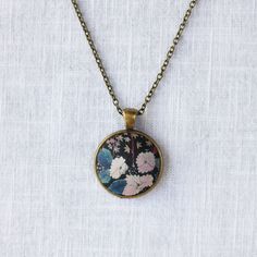 Inspired by Liberty Art Fabric, I developed my collection of vintage-style jewellery. The vibrant floral motifs of Liberty fabric are truly celebrated and showcased in this collection. A great gift for nature-lovers that will never go out of fashion. This necklace features white flowers in the dark background which has an oriental painting feeling. It has an antique bronze alloy pendant tray and an oval pendant. The long brass chain has a lobster clasp and a tiny bee beside it. Pendant 2.8 x 2.8 Vintage Brass Jewelry With Flower Charm, Vintage Multicolor Necklace With Adjustable Chain, Vintage Brass Flower Jewelry, Vintage Multicolor Pendant Necklaces, Vintage Multicolor Jewelry With Flower Charm, Vintage Multicolor Jewelry With Large Pendant, Multicolor Brass Elegant Necklaces, Elegant Multicolor Brass Necklaces, Nature-inspired Multicolor Round Jewelry