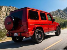 a red mercedes g class driving down the road