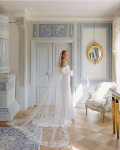 a woman in a white wedding dress is standing near a chair with a veil on her head