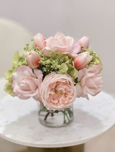 a vase filled with pink flowers sitting on top of a white table next to a chair