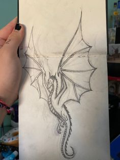 a drawing of a dragon is being held up by a person's hand in front of a computer screen