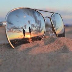 two people are reflected in the mirrored sunglasses on the sand at sunset or sunrise,