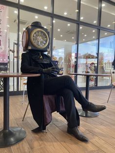 a man sitting on top of a wooden table wearing a clock face mask and black pants