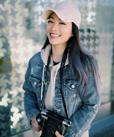 a young woman holding a camera and smiling at the camera with her hat on top of her head