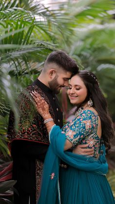 a man and woman standing next to each other in front of palm trees with their arms around each other