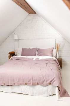 a bed with pink sheets and pillows in a loft space under a slanted ceiling