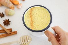 a person holding a cup of coffee with cinnamons and anise on the side