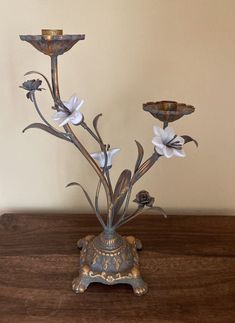 a metal vase with flowers in it sitting on a wooden table next to a wall