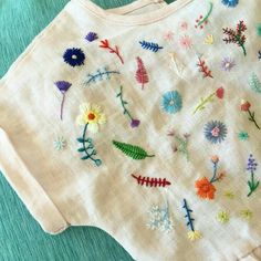 a white shirt with colorful embroidered flowers on it's chest and sleeves, sitting on a green surface