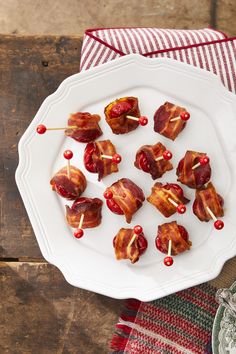 bacon wrapped in toothpicks on a white plate next to a red and white napkin