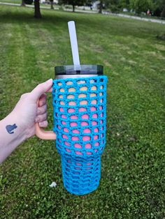 a hand holding a blue plastic cup with a straw in it on top of green grass