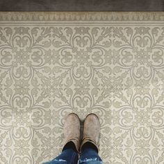 someone's feet in jeans and slippers standing on a tile floor next to a wall