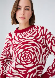 a woman wearing a red and white sweater with a rose pattern on the side, standing in front of a white background