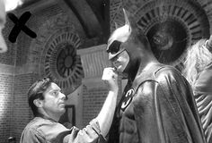 a man is shaving the face of a batman statue in front of another man