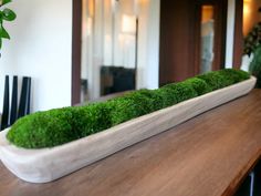 a wooden table topped with a white vase filled with green moss