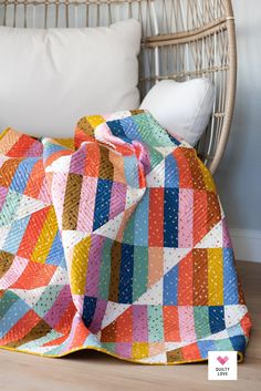 a colorful quilt sitting on top of a wooden floor next to a white pillow and wicker chair