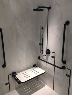 a bathroom with white marble walls and black fixtures on the shower head, toilet seat and hand rail