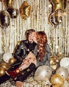 a man and woman sitting next to each other in front of gold foiled balloons